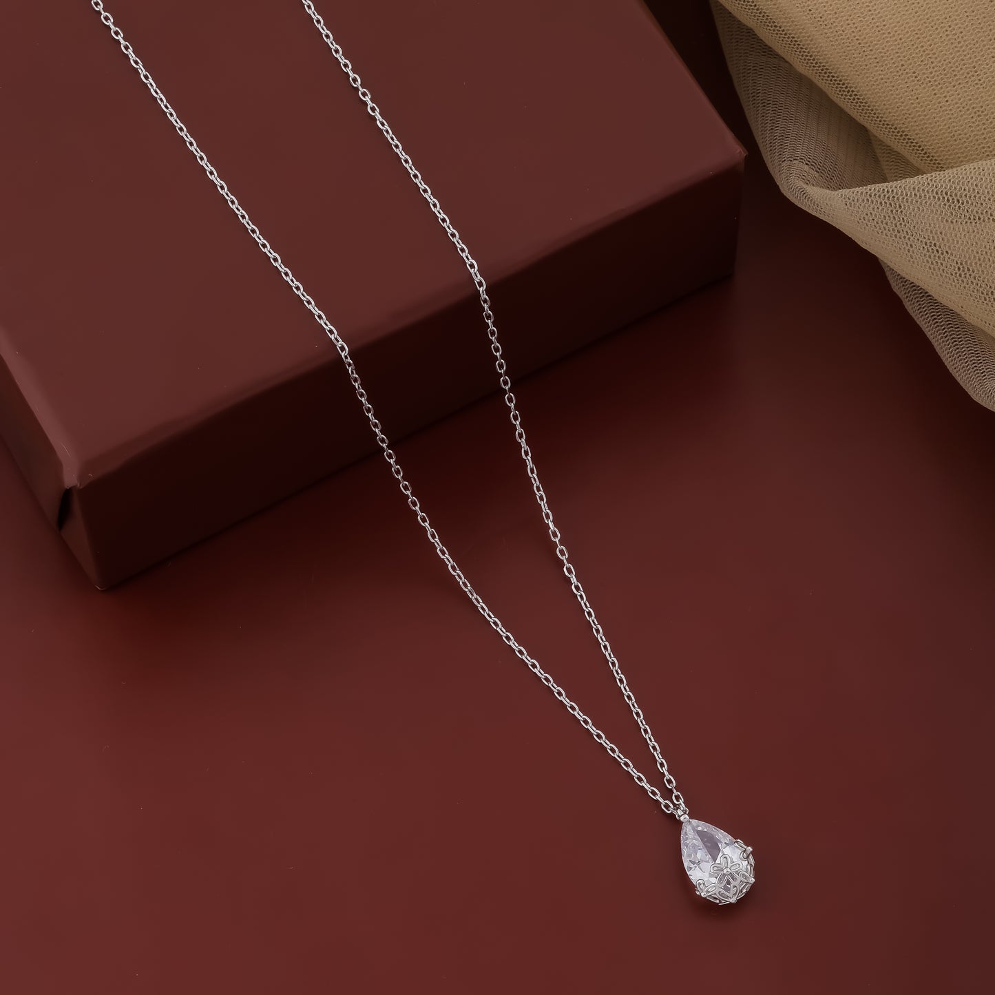 Silver necklace with a teardrop pendant on a brown surface