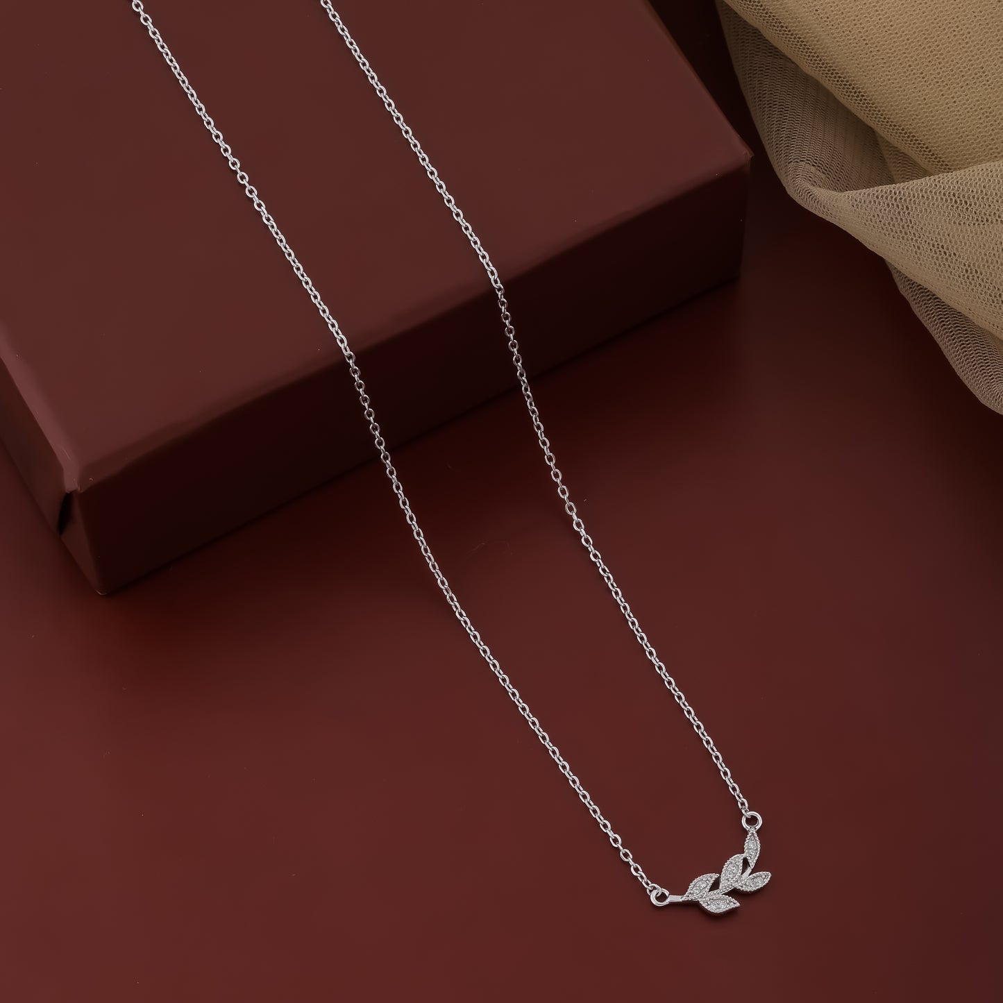 Silver necklace with leaf pendant on a brown surface