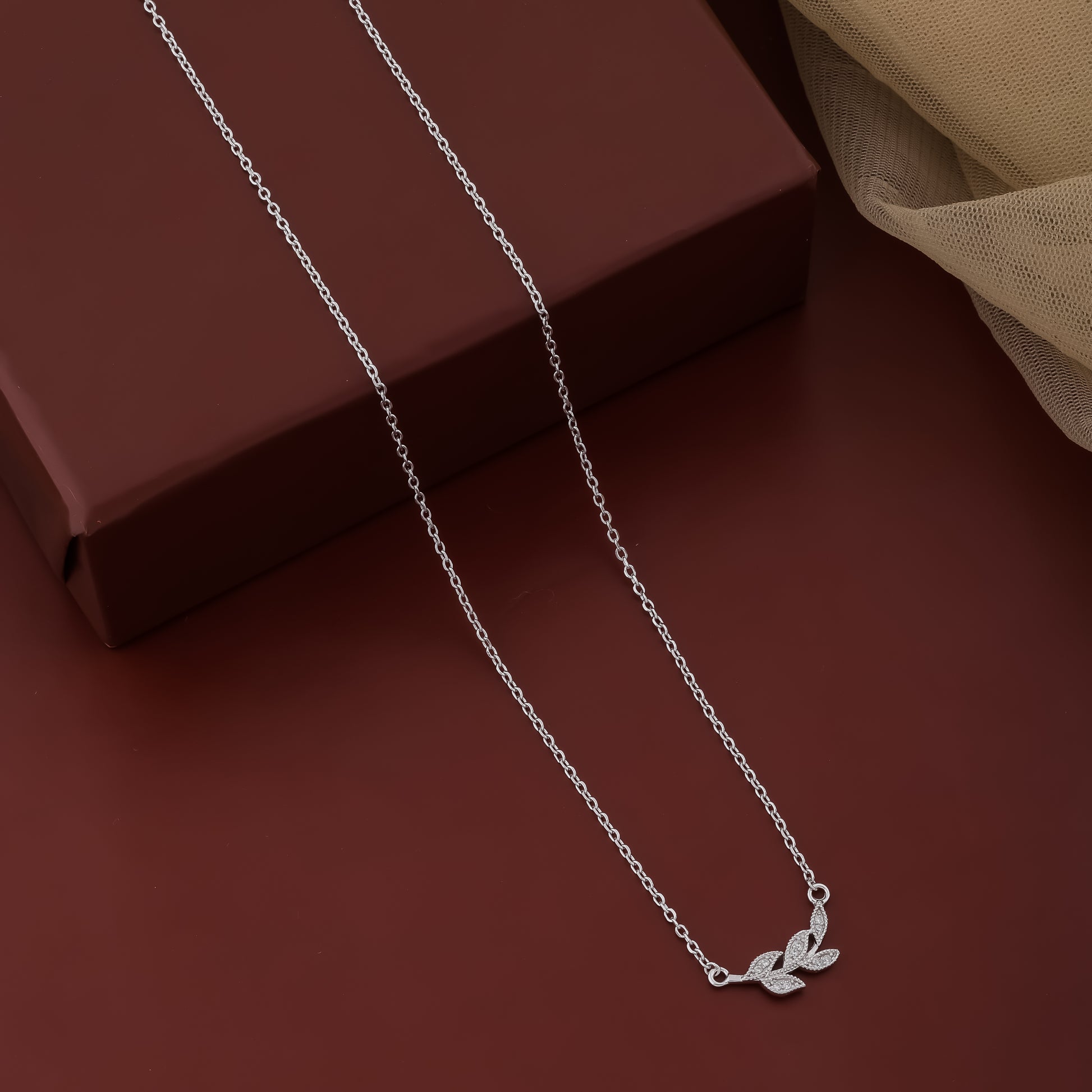 Silver necklace with leaf pendant on a brown surface