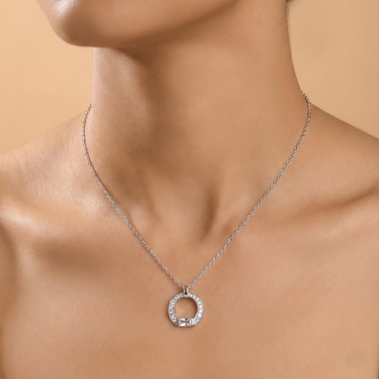 Silver necklace with a circular pendant on a person's neck against a beige background