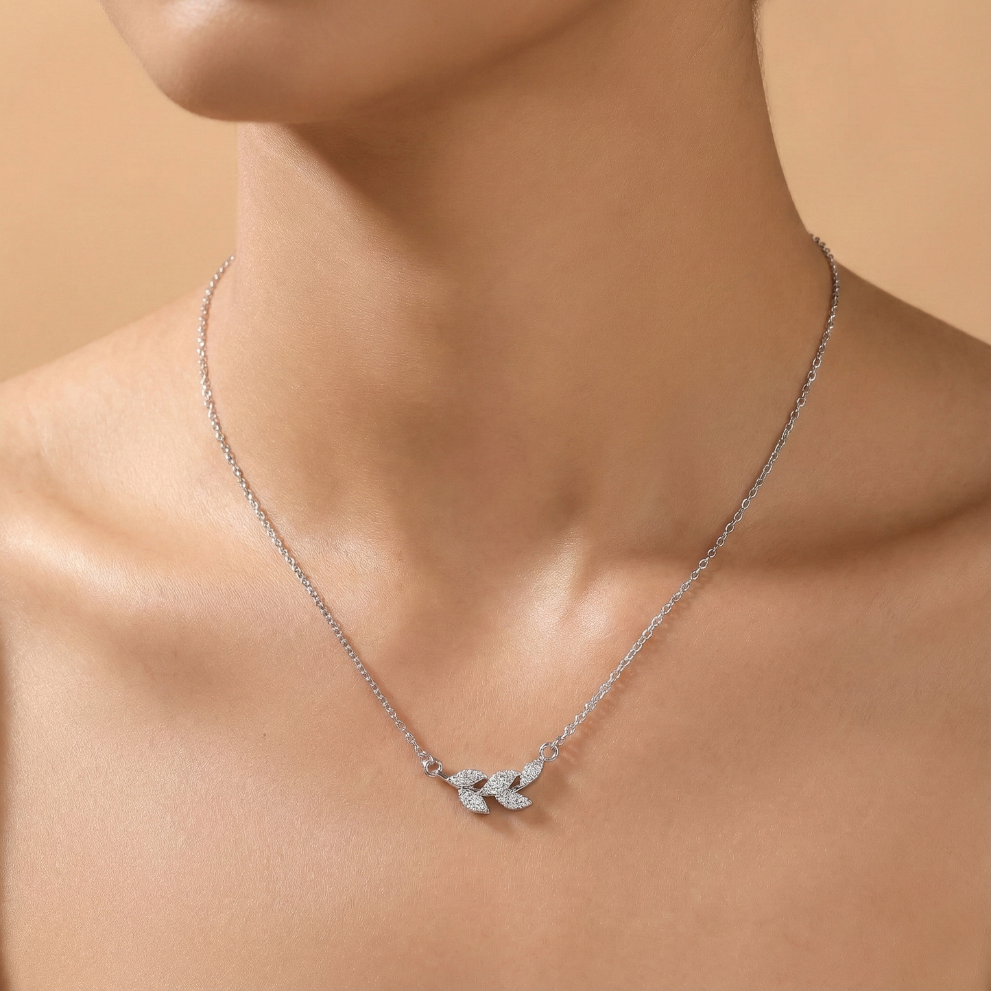 Silver necklace with a leaf pendant on a person against a beige background