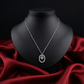 Silver necklace with a pink gemstone pendant on a black mannequin bust against a red fabric background