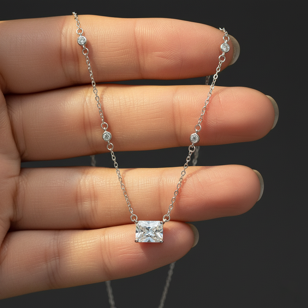 Silver necklace with a square pendant held between fingers against a dark background