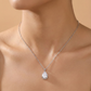 Silver necklace with a teardrop-shaped pendant on a person against a beige background
