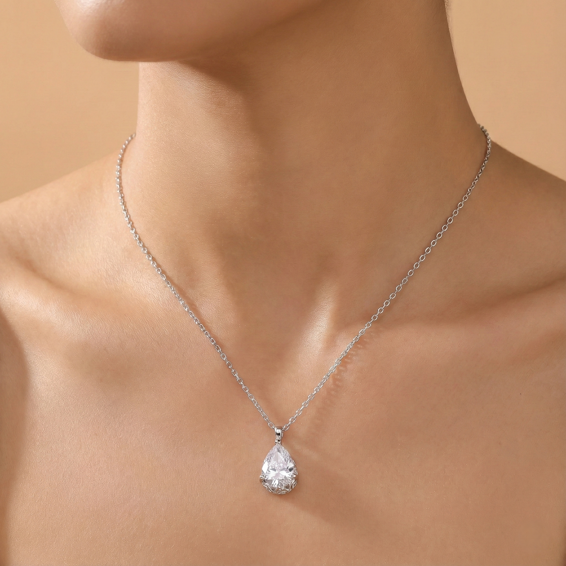 Silver necklace with a teardrop-shaped pendant on a person against a beige background