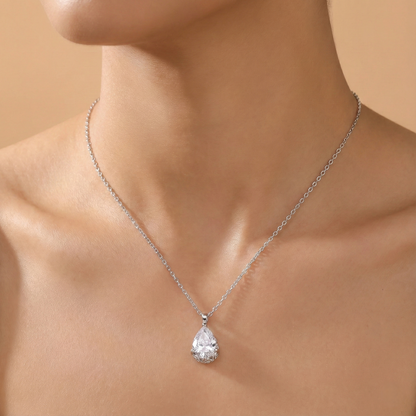 Silver necklace with a teardrop-shaped pendant on a person against a beige background