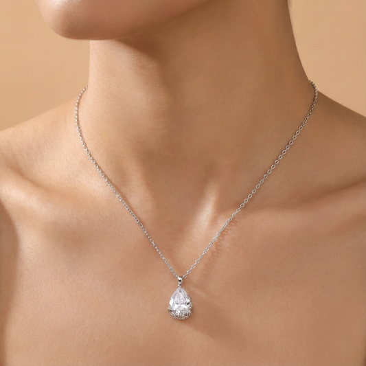 Silver necklace with a teardrop-shaped pendant on a person against a beige background