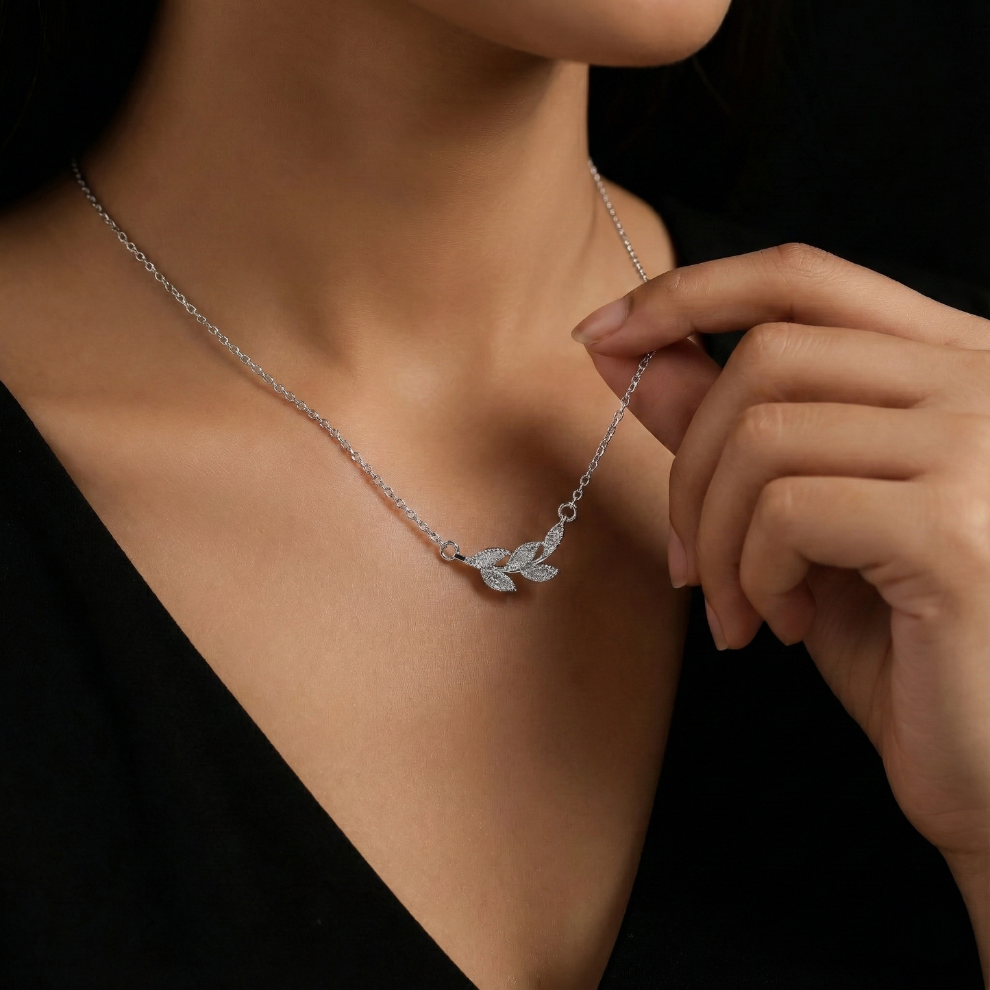 Silver necklace with leaf design worn by a person against a black background