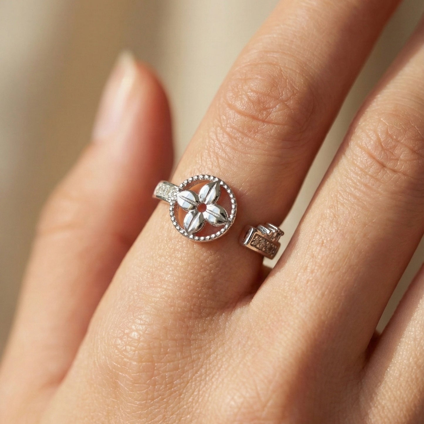 Silver ring with floral design on a hand against a neutral background