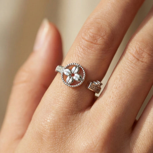 Silver ring with floral design on a hand against a neutral background