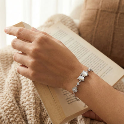 Hand wearing a silver bracelet with a heart charm, holding an open book against a soft, blurred background.