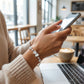 Person using a smartphone in a cafe setting with a laptop and coffee cup on the table.