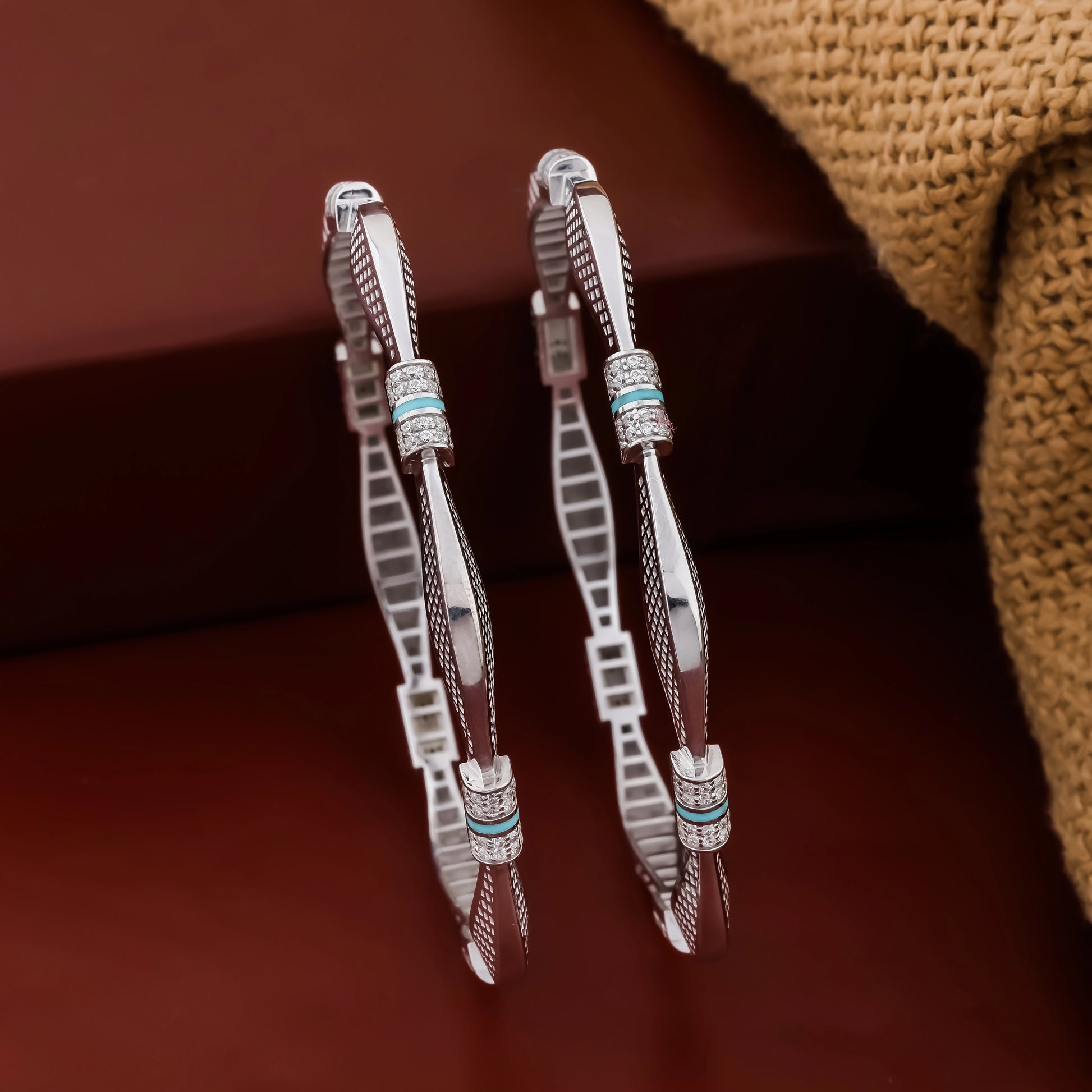 Pair of silver bangles with feather designs on a brown background