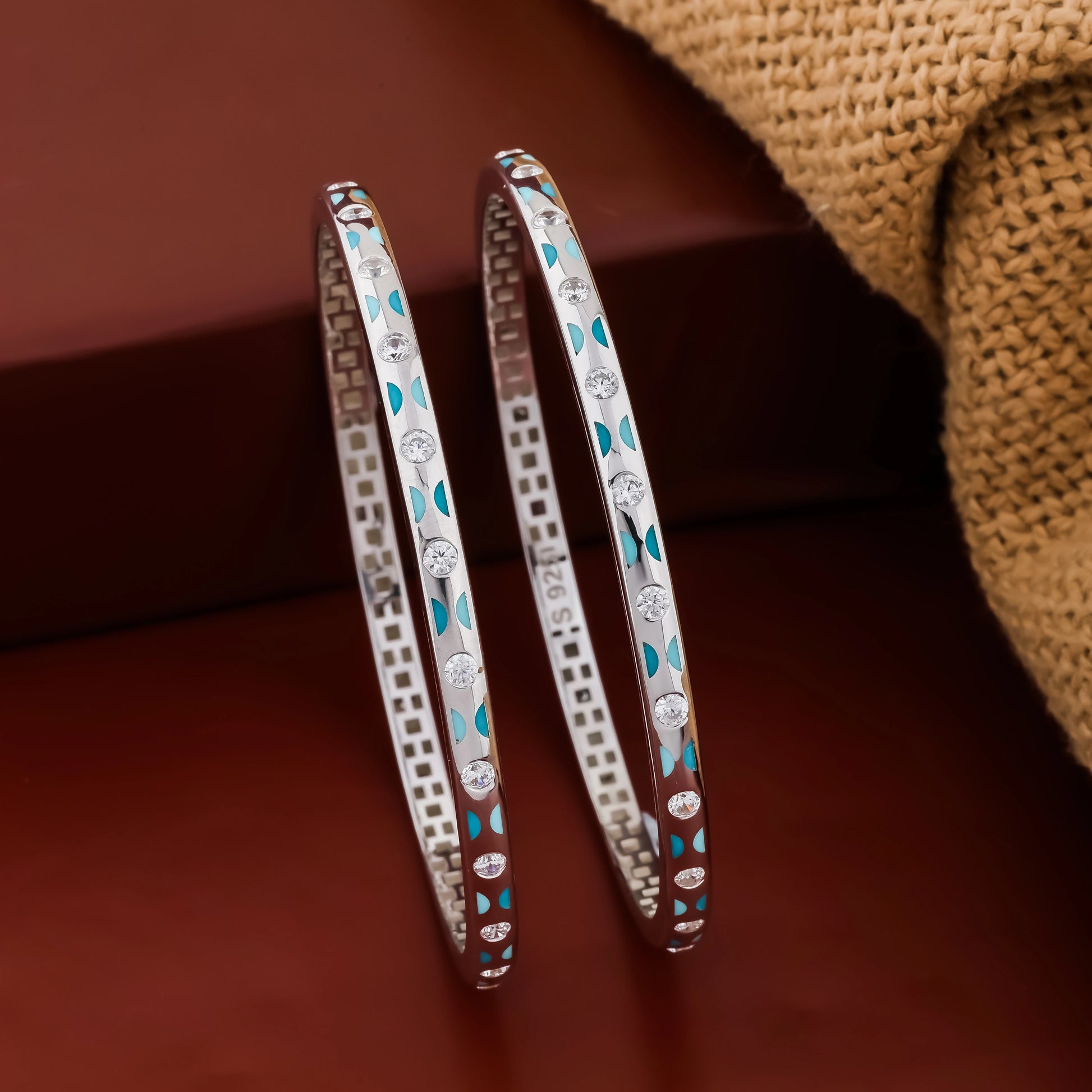 Pair of silver bangles with turquoise stones on a brown background