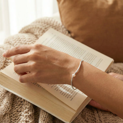 Person reading a book with a bracelet on wrist, cozy indoor setting