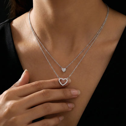 Two silver necklaces with heart pendants on a person wearing a black top.