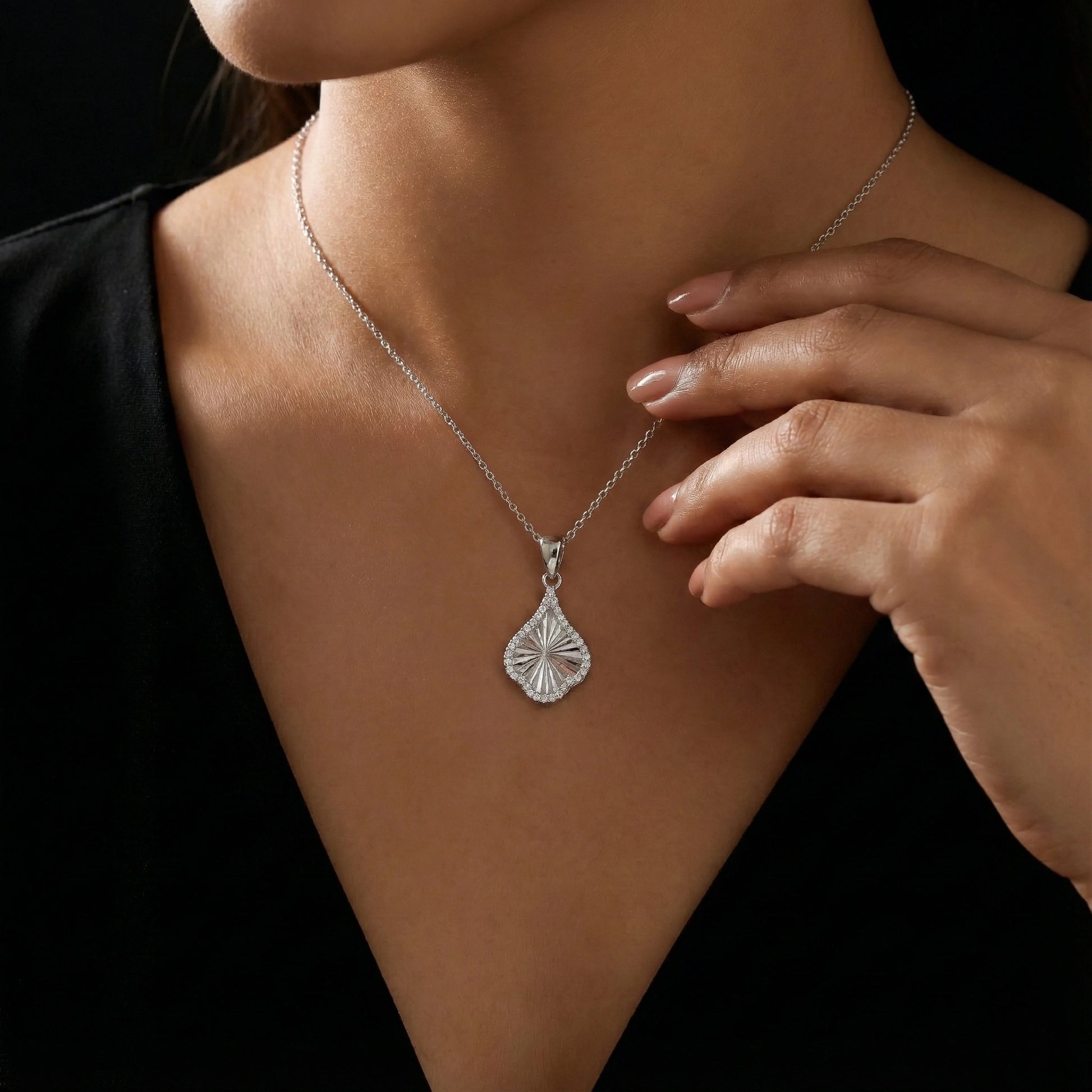 Silver necklace with a pendant worn by a person against a black background