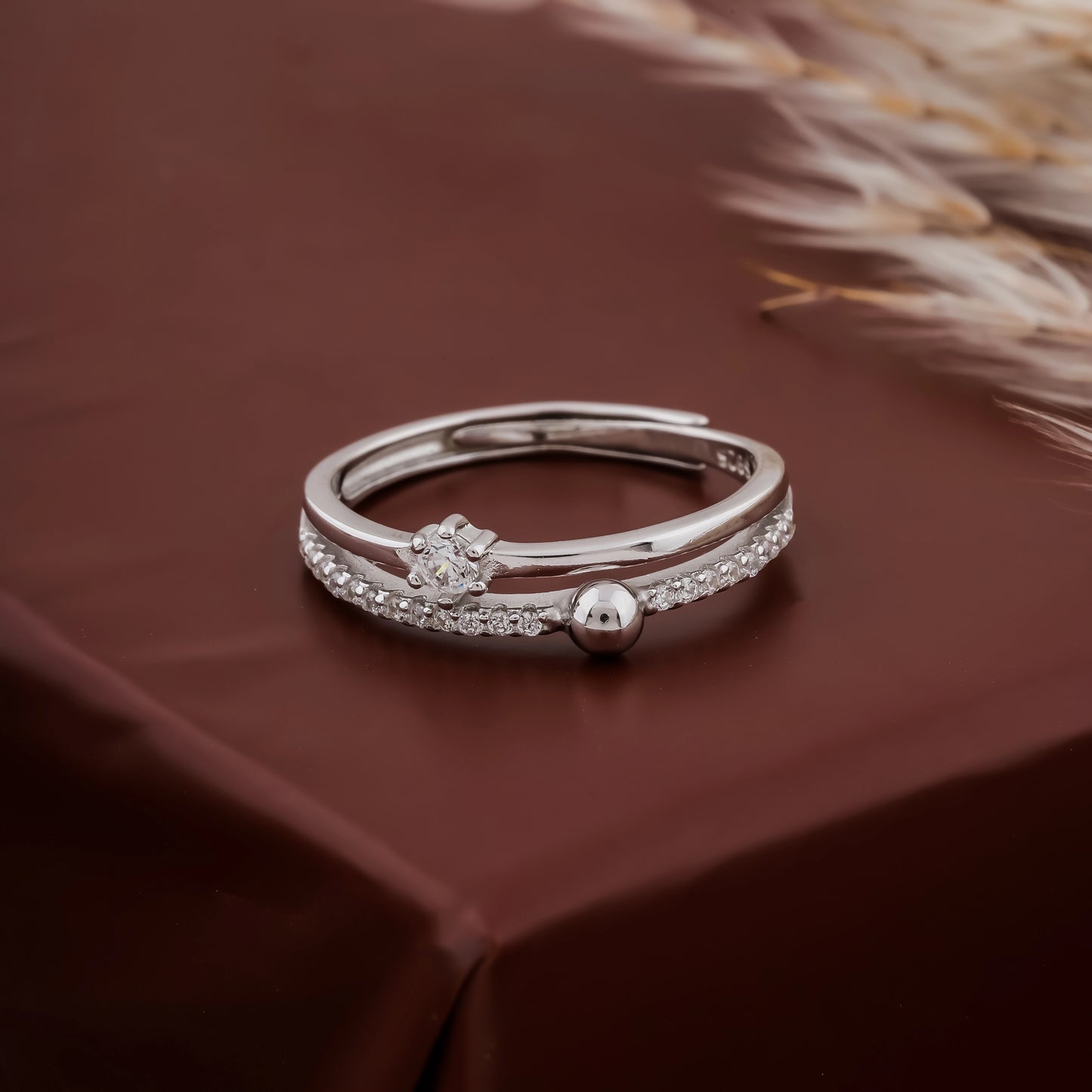 Silver ring with small ball and decorative elements on a brown fabric background