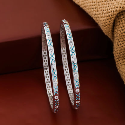 Two silver bangles with blue gemstones on a brown fabric background