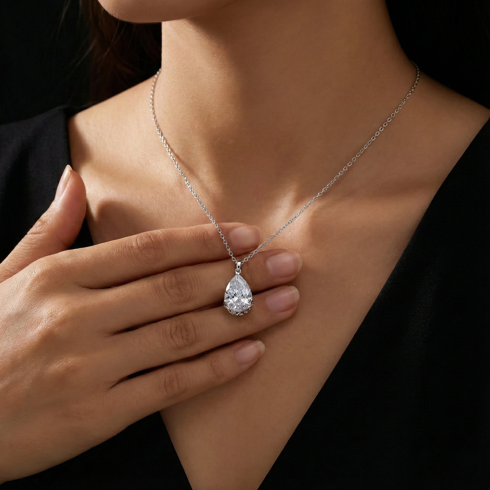 Teardrop-shaped diamond pendant on a necklace worn by a person against a black background