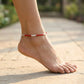 Foot wearing a red beaded anklet on a blurred outdoor background