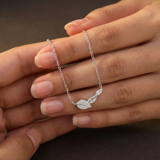 Silver necklace with a leaf pendant held between two fingers against a dark background