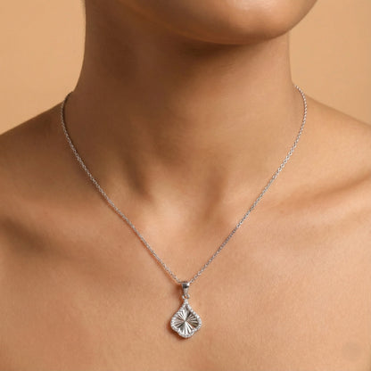 Silver necklace with a pendant on a person against a beige background