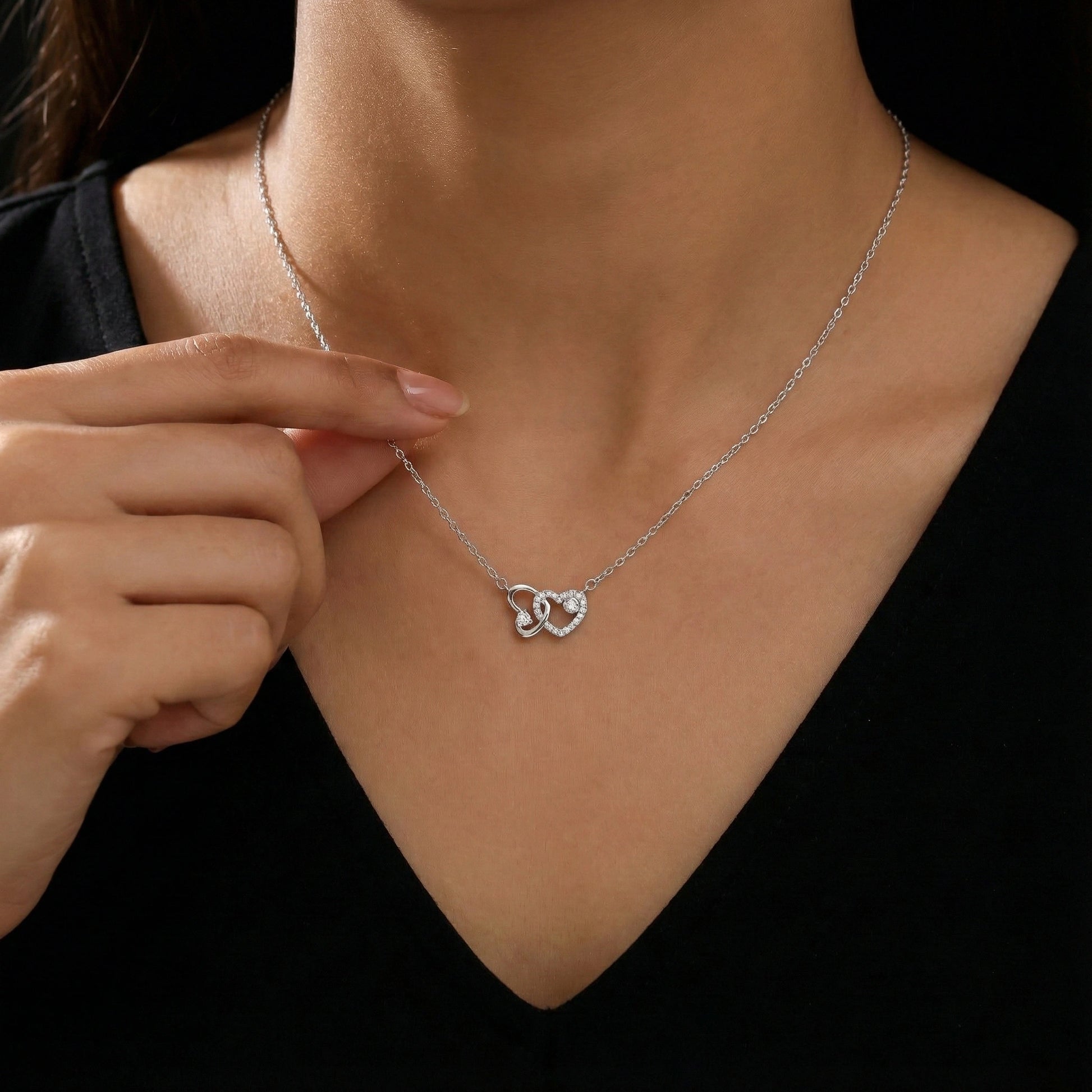 Silver necklace with a heart-shaped pendant worn by a person against a black background