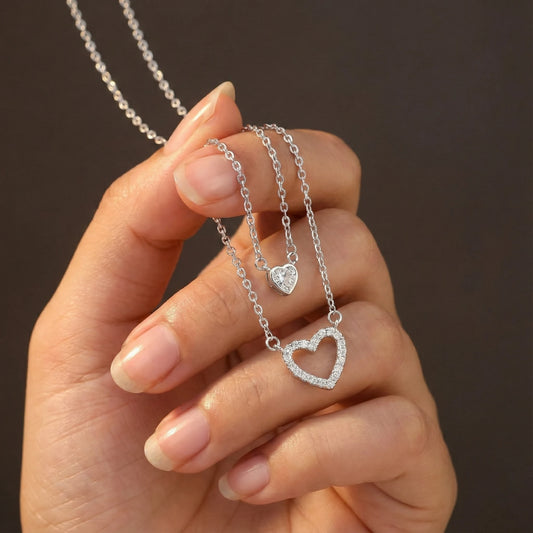 Hand holding two silver heart-shaped necklaces against a dark background