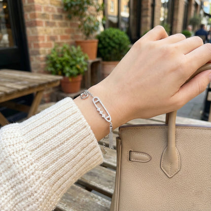 Hand holding a beige handbag with a silver bracelet on a blurred street background
