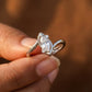 Silver ring with a pear-shaped diamond held in a hand against a blurred brown background