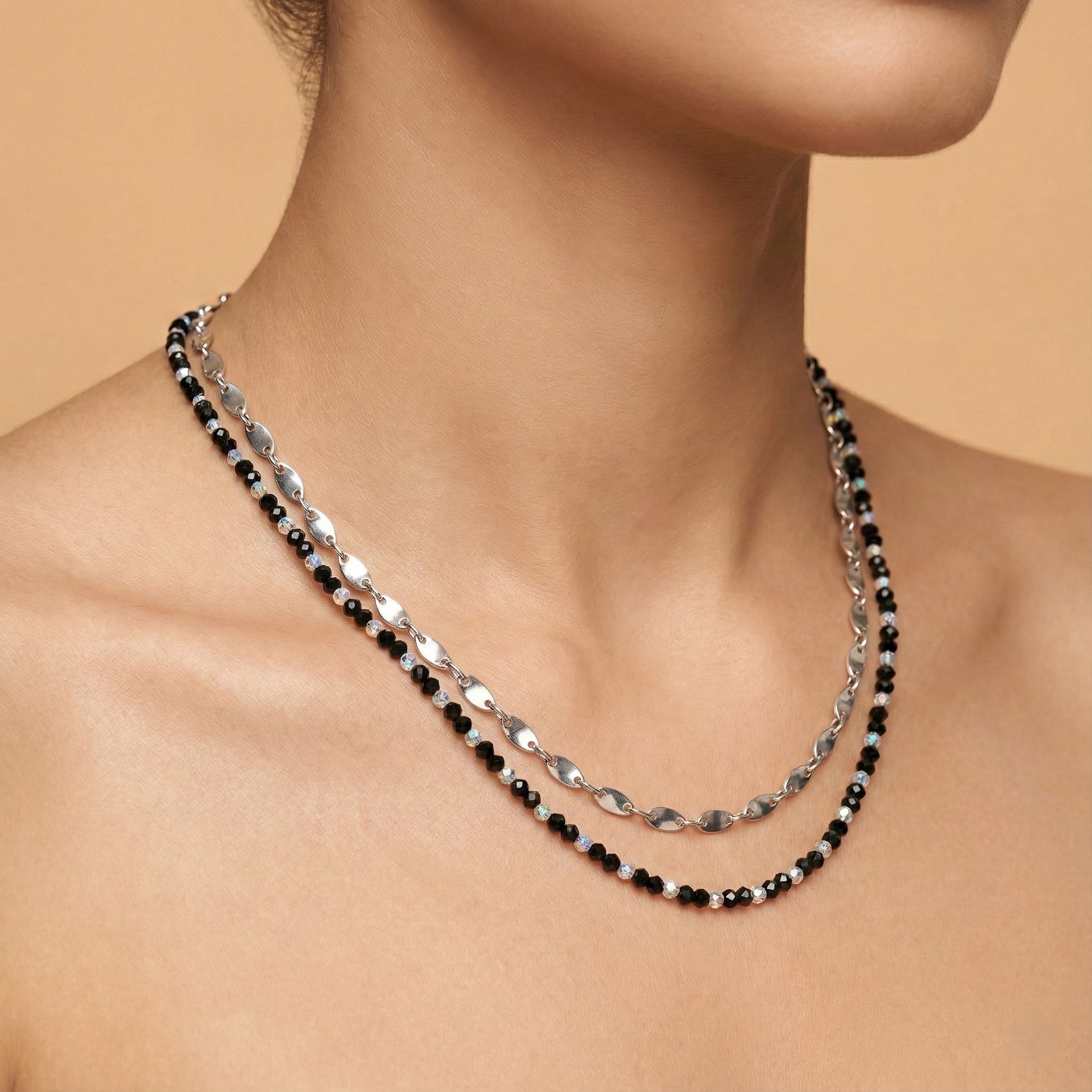 Necklace with black and silver beads on a person against a beige background