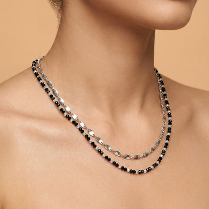 Necklace with black and silver beads on a person against a beige background