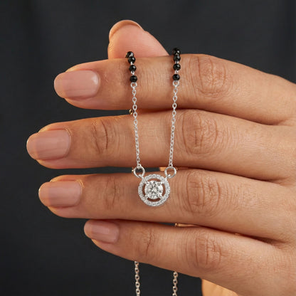 Hand holding a silver necklace with a round pendant against a dark background