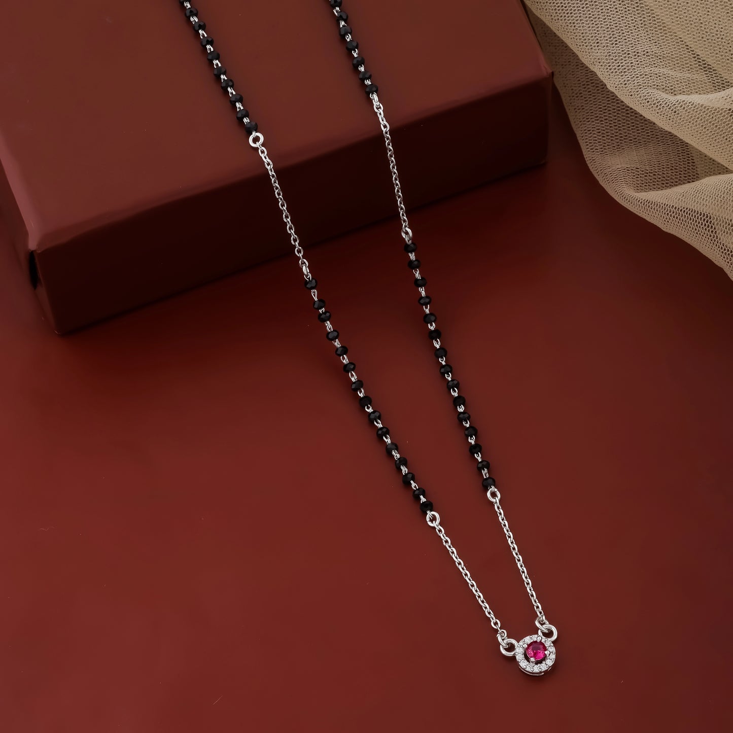 Silver necklace with a red gemstone pendant on a brown surface