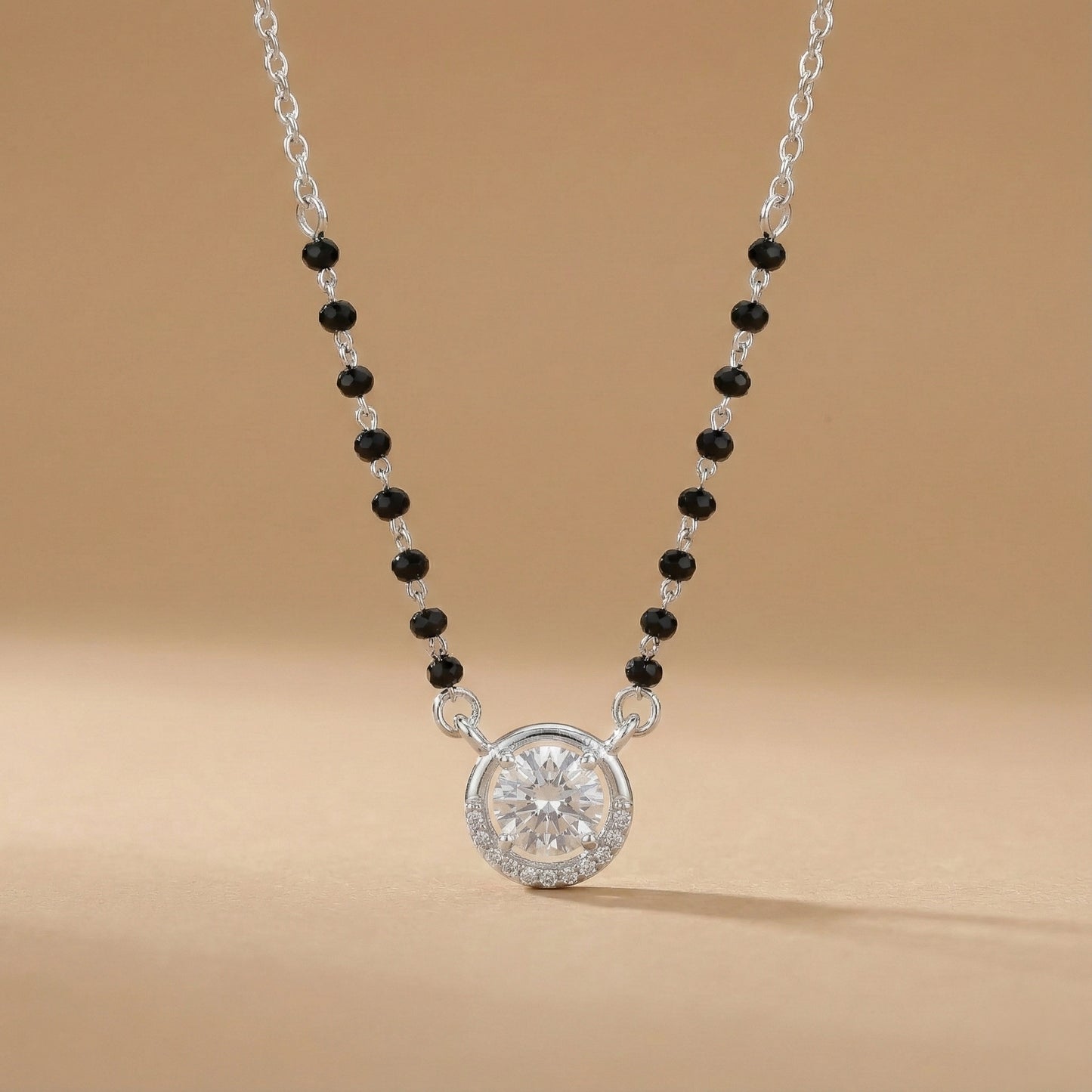 Necklace with black beads and a silver pendant on a beige background