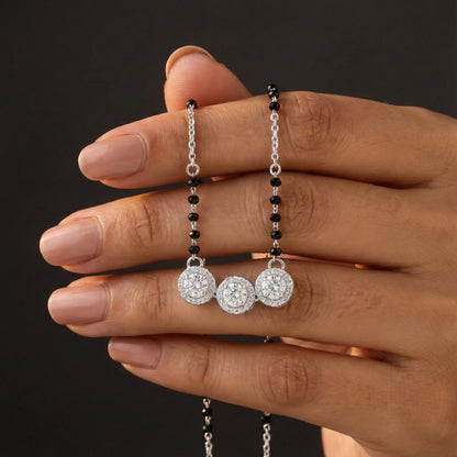 Hand holding a pair of silver earrings with black beads against a dark background