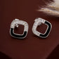 Pair of silver hoop earrings with black accents on a brown background