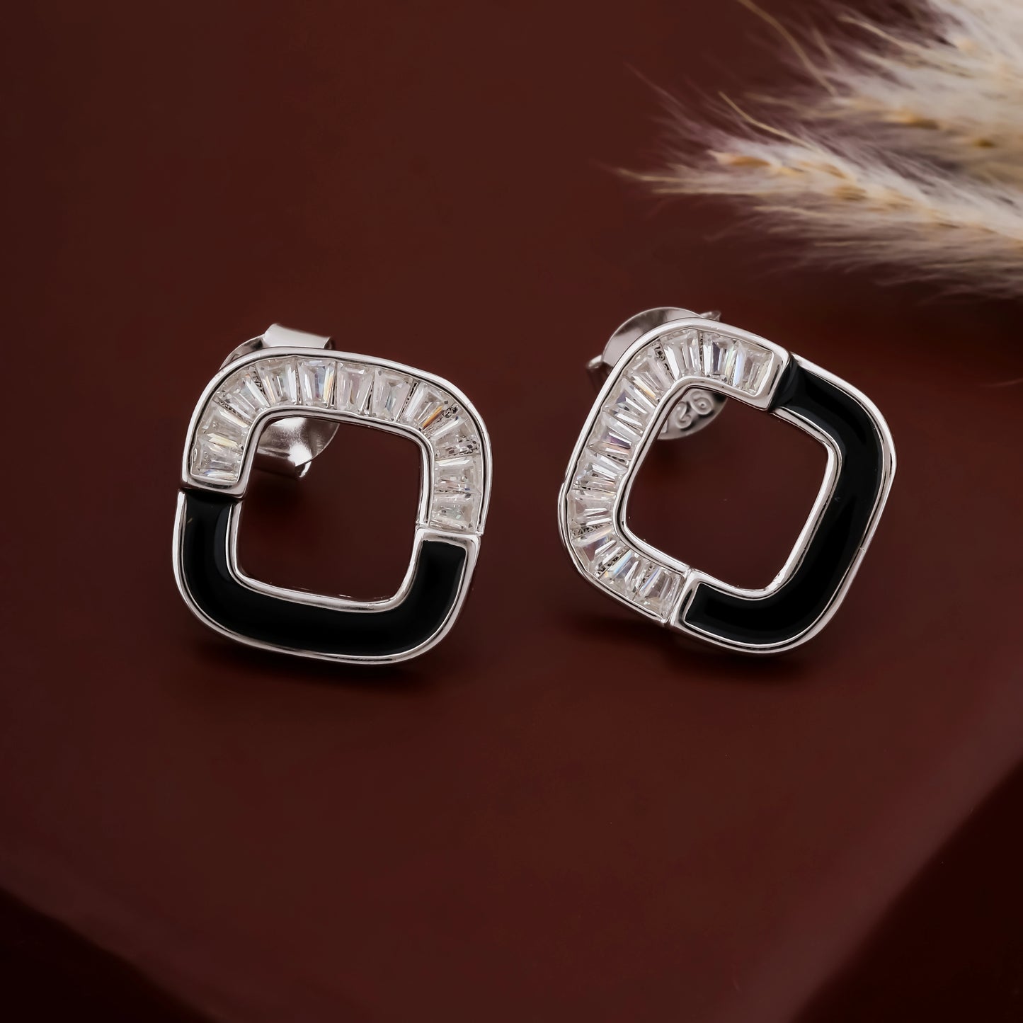 Pair of silver hoop earrings with black accents on a brown background
