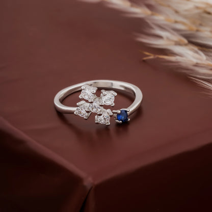 Silver ring with floral design and blue gemstone on a brown fabric background