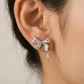 Silver bow-shaped earring worn on an ear with a neutral background
