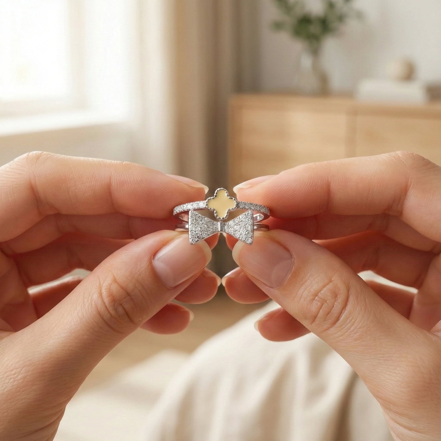 Two hands holding two rings with bow designs and a yellow gemstone.