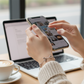 Person using a smartphone with a laptop and bracelet with coffee cup on a desk