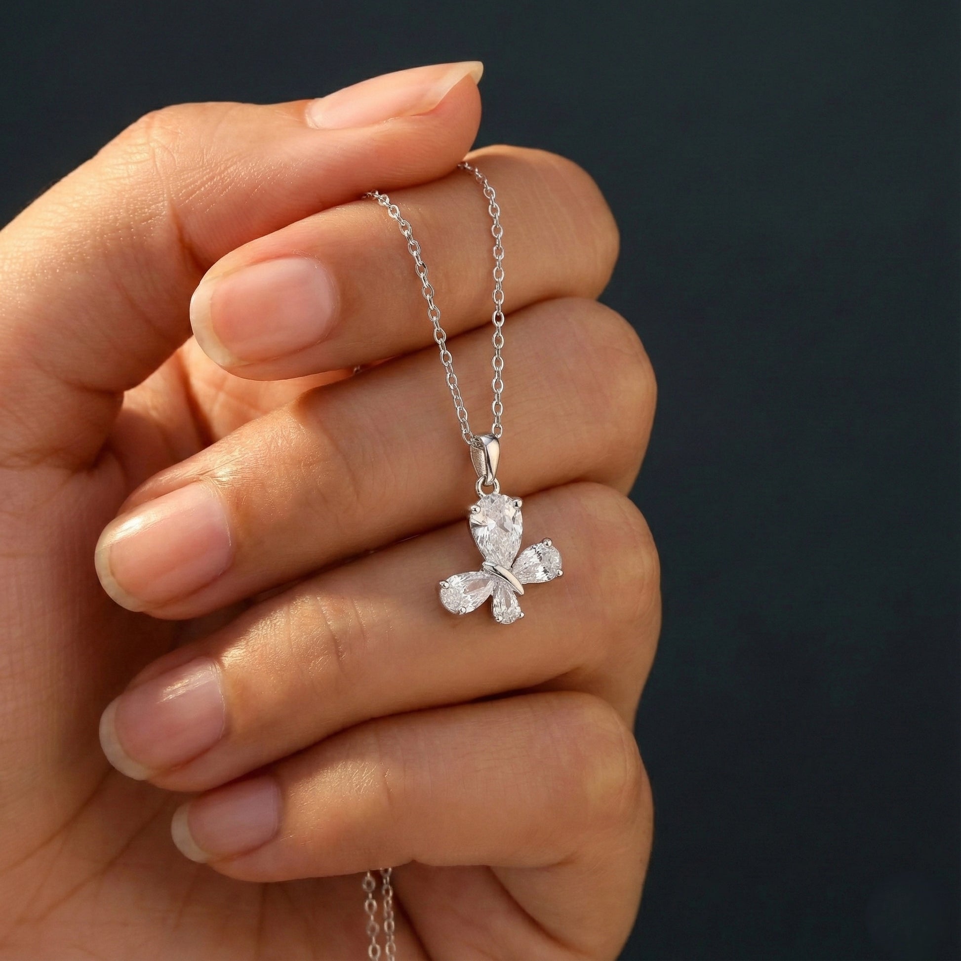Hand holding a silver necklace with a clover-shaped pendant against a dark background