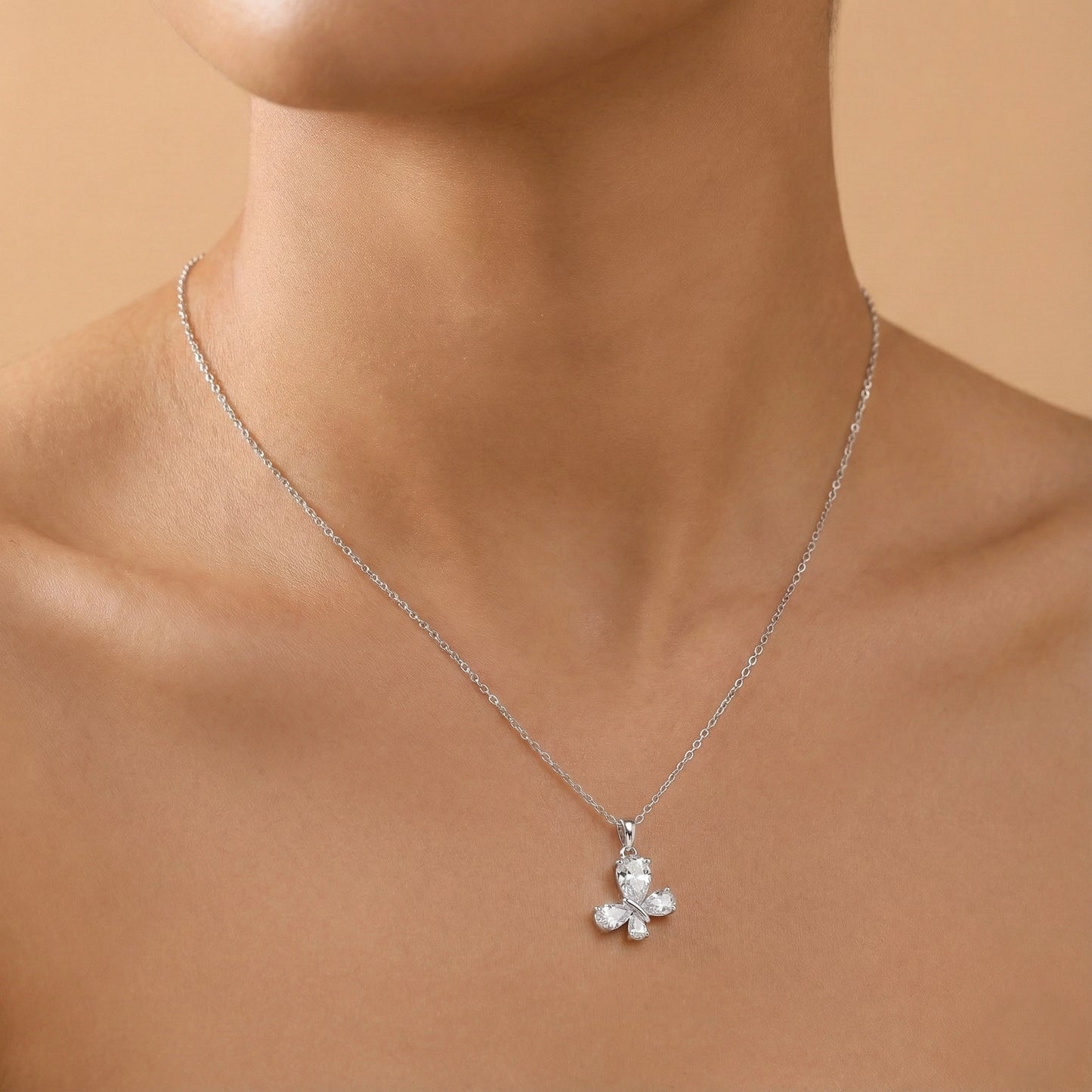 Silver necklace with a teddy bear pendant on a person's neck against a beige background