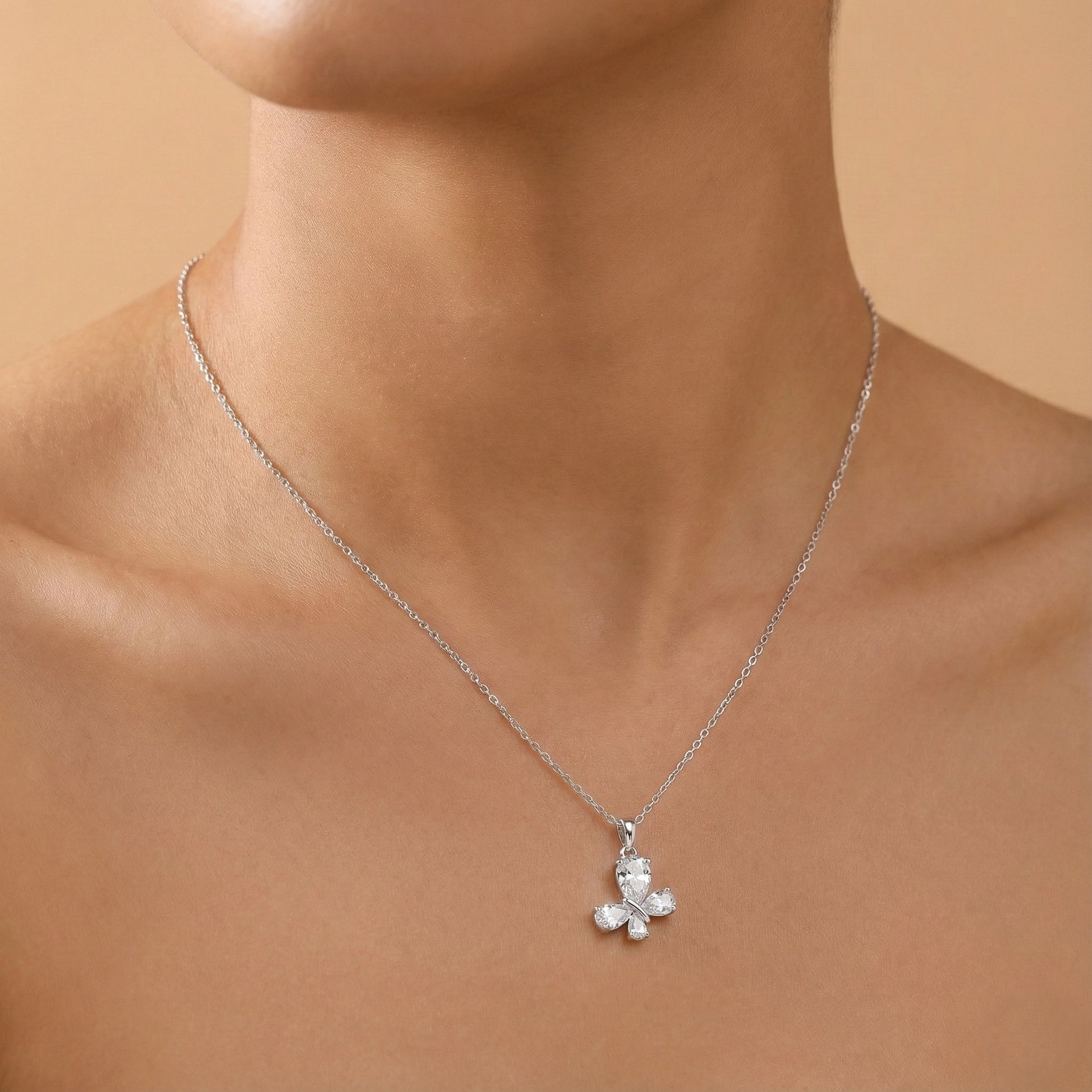 Silver necklace with a teddy bear pendant on a person's neck against a beige background