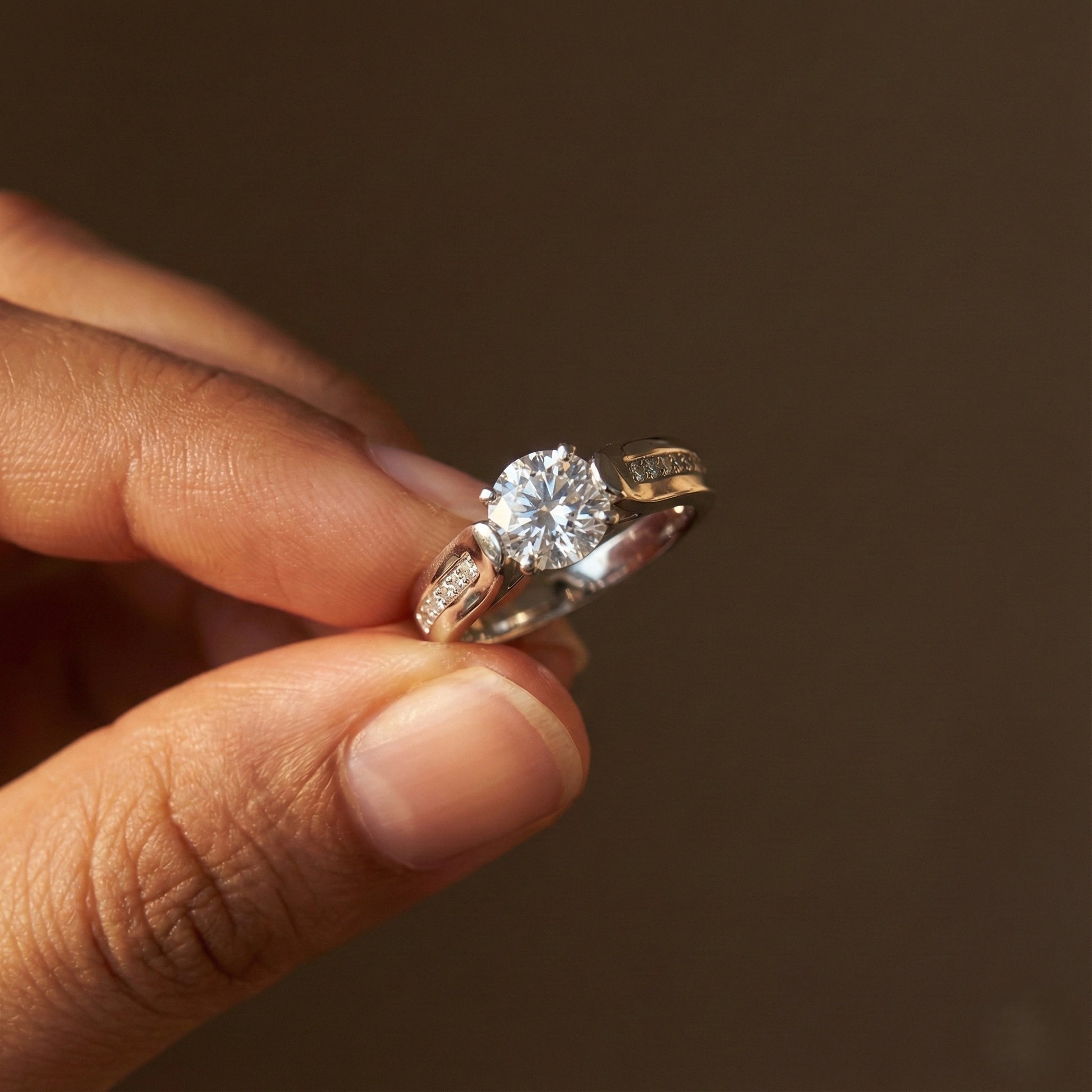 Close-up of a hand holding two diamond rings against a dark background