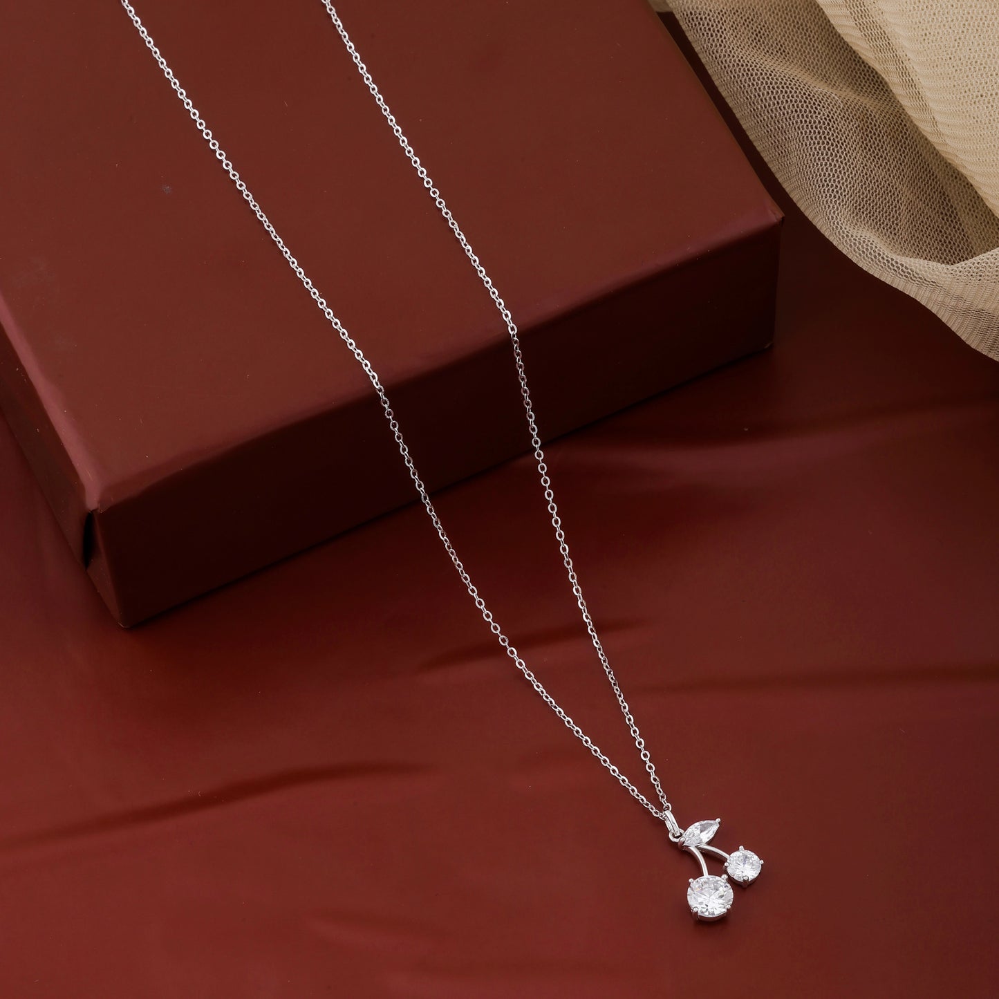 Silver necklace with a cherry pendant on a red surface