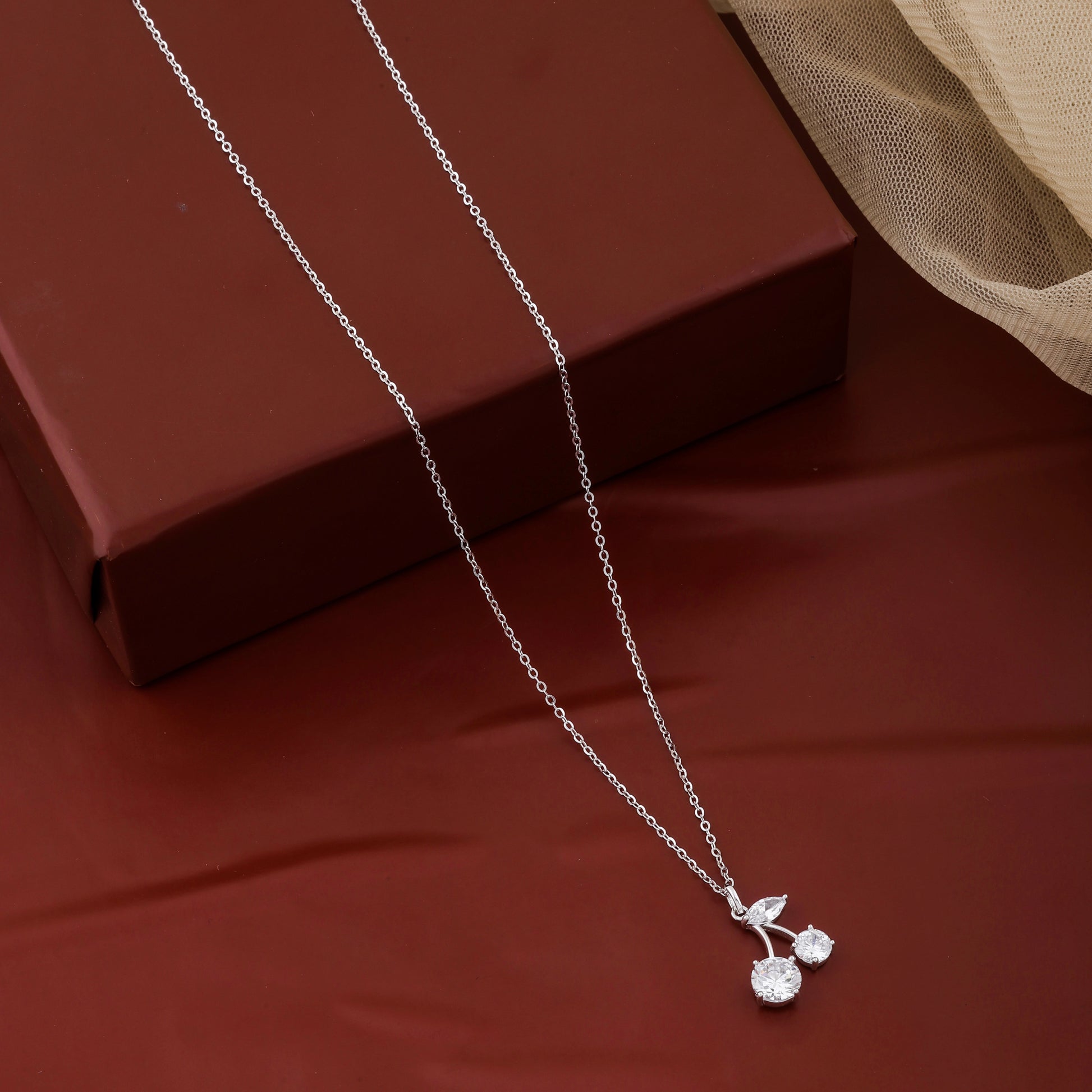 Silver necklace with a cherry pendant on a red surface