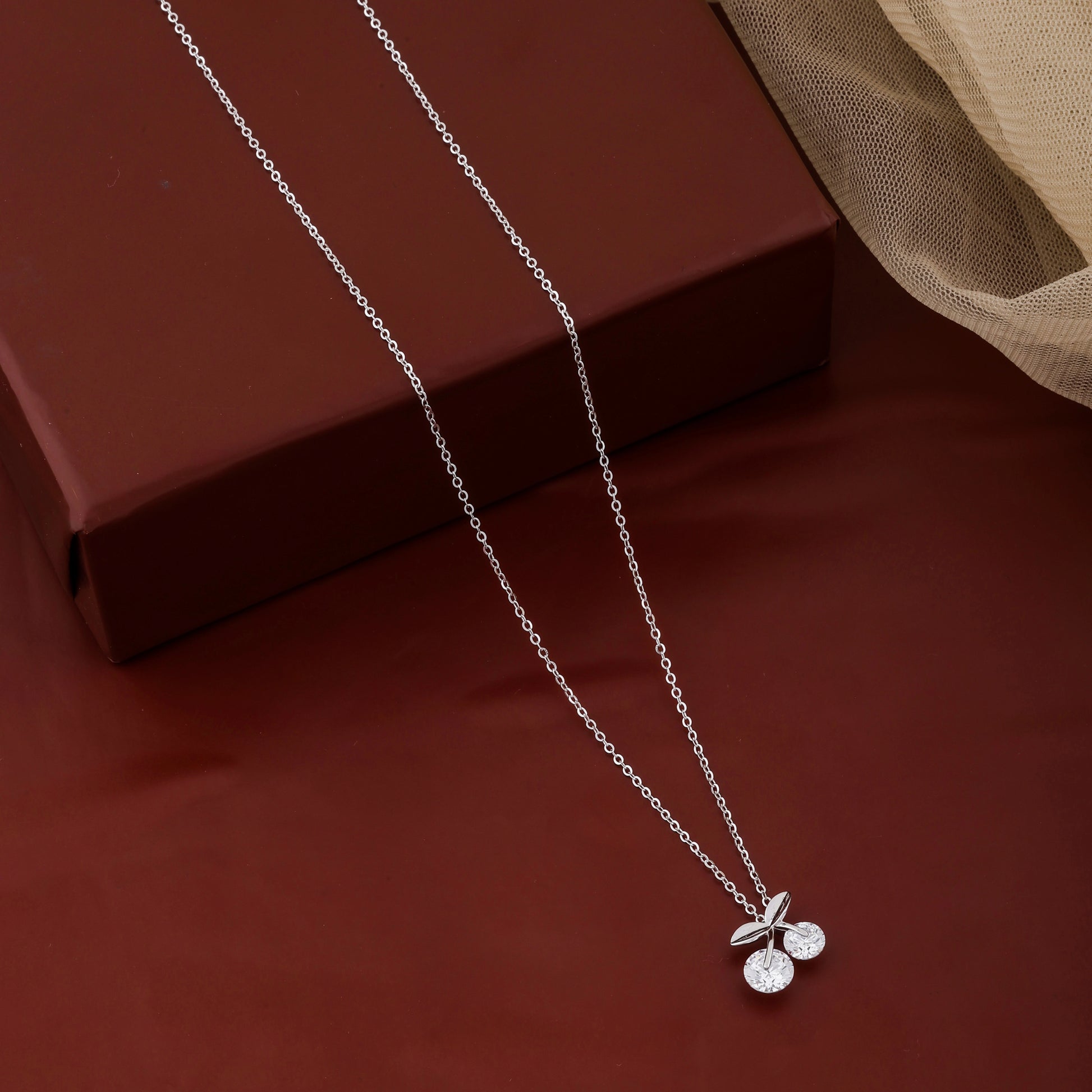 Silver necklace with a cherry pendant on a red surface
